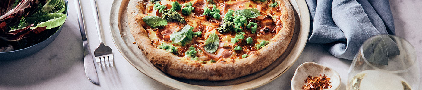 Green pea and pancetta pizza on table with salad, knife, fork, wine and serviette