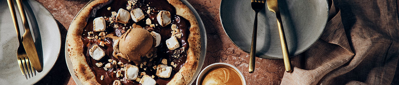 Roast Hazelnut, icecream and chocolate pizza with person holding coffee and plates on a table