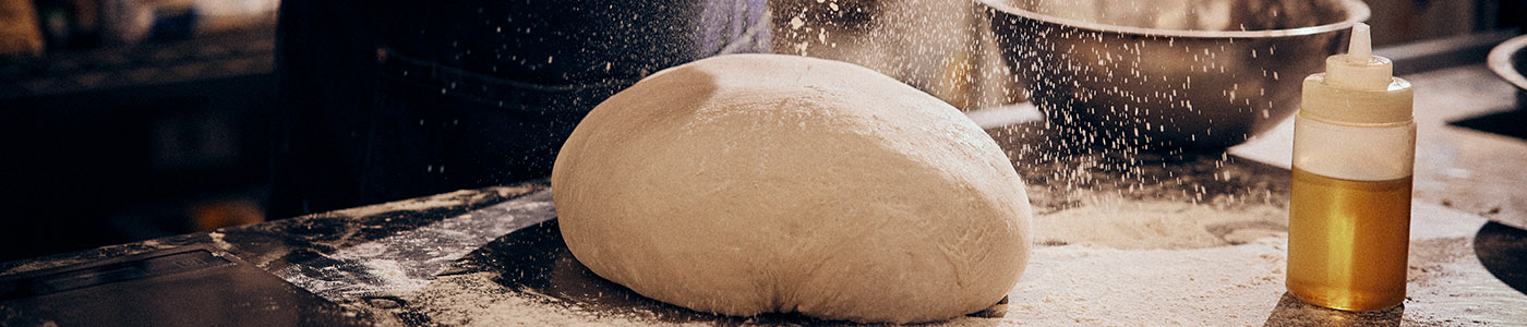 Marble bench with pizza dough balls flour and a pizza base being rolled out in the background