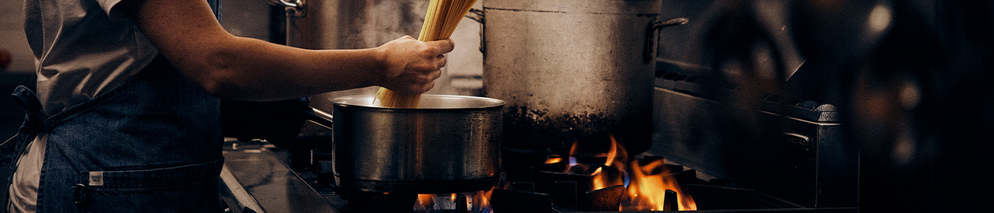 Chef putting spahetti into steaming pot in commercial kitchen