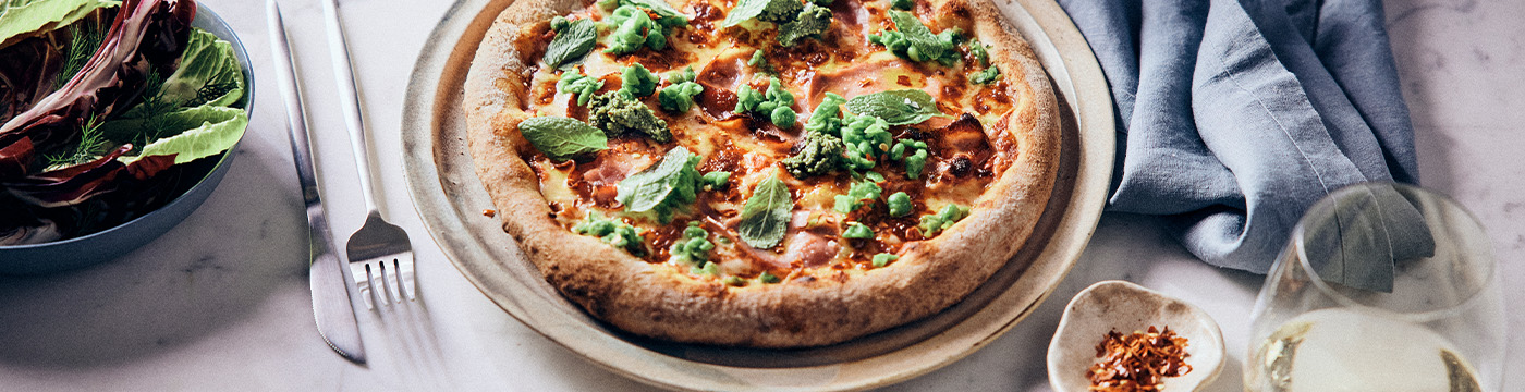 Pizza with green peas and pancetta at a restaurant table setting