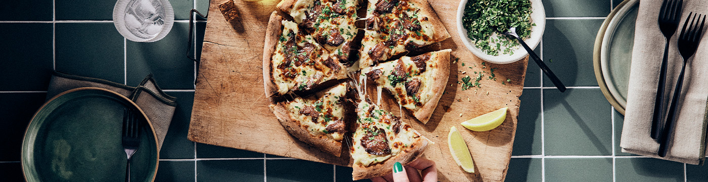 Braised beef cheek pizza sliced on a chopping board with lemon wedges